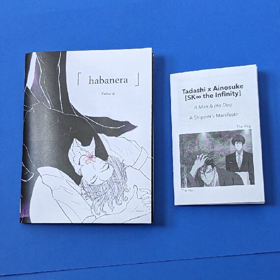 Two zines on a blue background: On the left: Habanera: On the right: Tadashi x Ainosuke SK8 the Infinity A Man & His Dog A Shipper's Manifesto.
